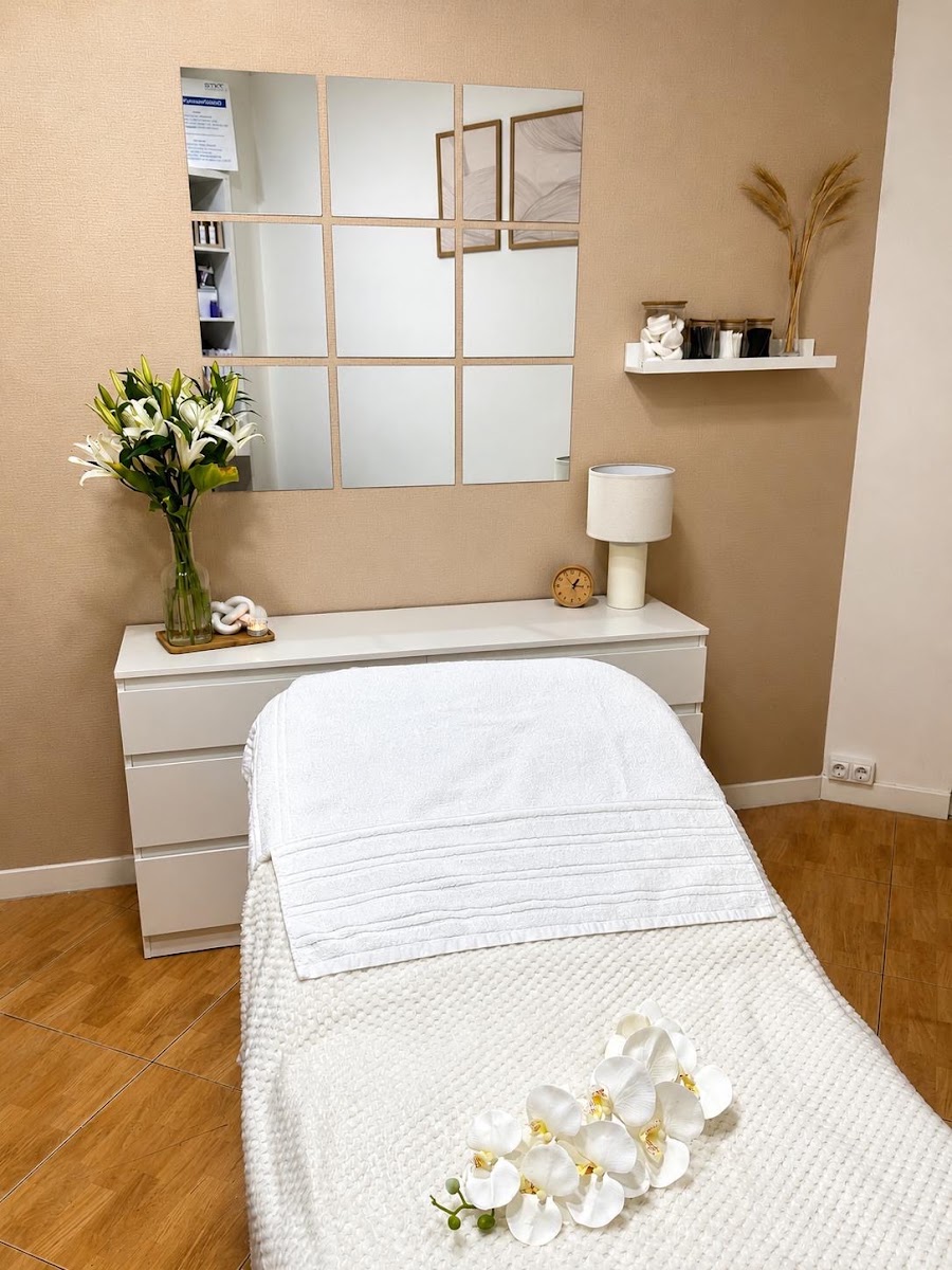 Cabina con camilla blanca, paredes beige, espejos en mosaico y flores